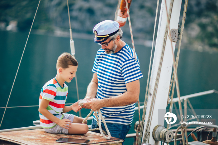 Senior man tying knot and securing with grandson on yacht sail boat.