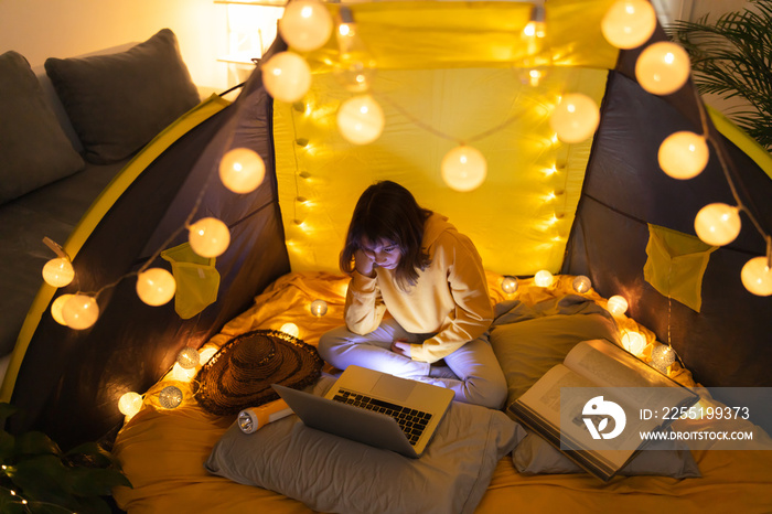 Little 11 year old girl using laptop under her home-made tent inside the living room.