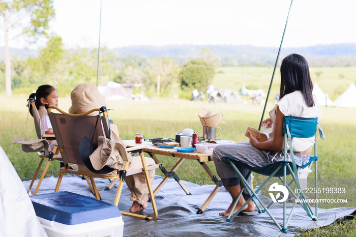 Happy family mother and daughters cooking and having breakfast while camping together at camping site. Family and outdoor activity concept.