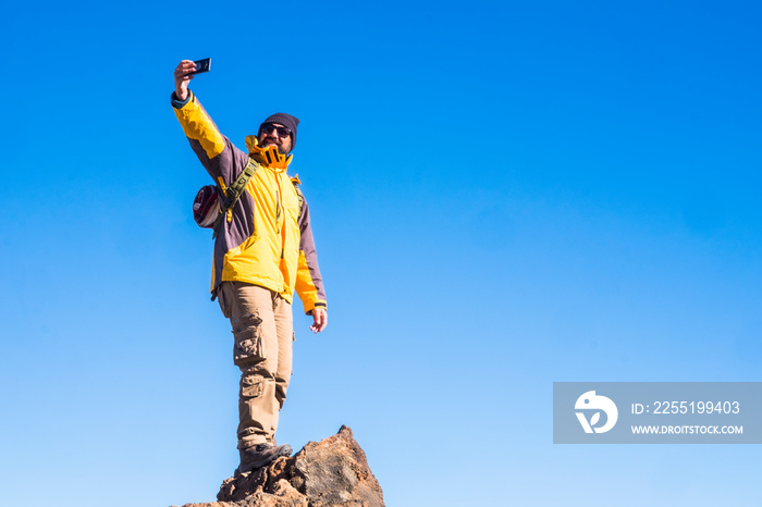 Adventure man standing outdoor on the top of a mountain with blue sky in background - concept of travel and trekking or hiking sport activity - people and technology outdoor