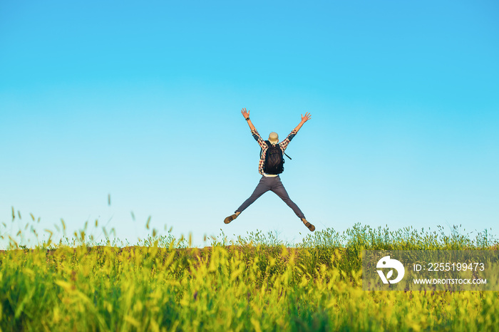 Rear view of man jumping up with outstretched arms, happy man with arms up against blue sky background, outdoors