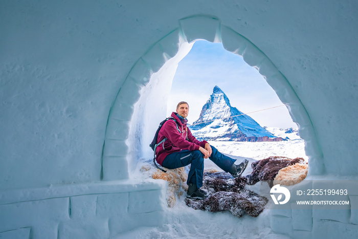 Portrait of man relaxing at entrance of igloo against Matterhorn in background