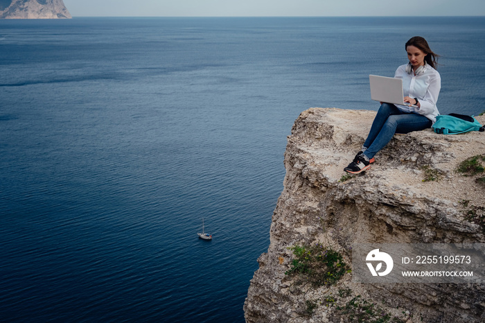 Young business woman working at the computer on the beach on the rock face.