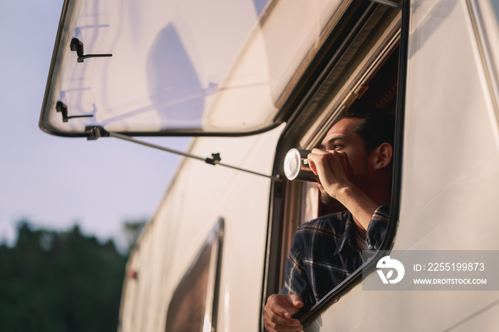 Handsome young Asian man, traveler on road trip, sit inside camping van in the morning. Cosy comfortable setup in camper trailer or van. Millennial travel trend, adventure on the road