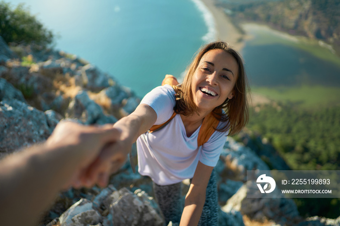 Outdoor portrait smiling girl hiker climbing up on cliff and holding helping hand for reaching to summit. Active lifestyle adventure concept