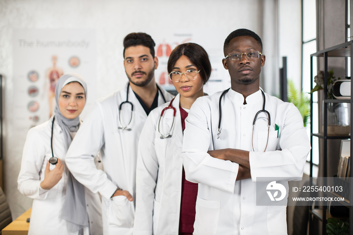 Confident medical specialists standing together at boardroom, smiling and looking at camera. Four diverse doctors posing indoors after successful meeting.