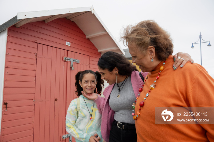 Grandmother, mother and granddaughter standing by red beach hut