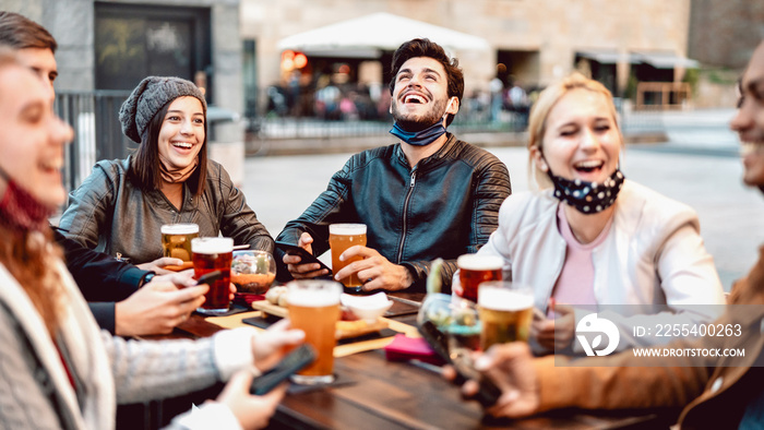 Young friends drinking beer wearing face mask - New normal lifestyle concept with people having fun together talking on happy hour at outside brewery bar - Bright warm filter with focus on central guy