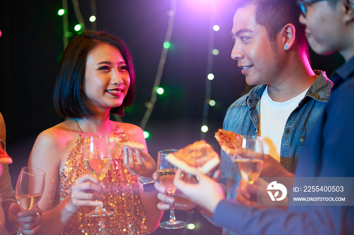 Group of young people drinking champagne and eating snacks at night party in club