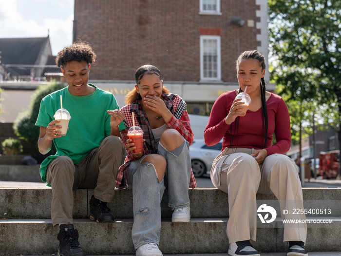 Friends laughing while drinking smoothies on steps