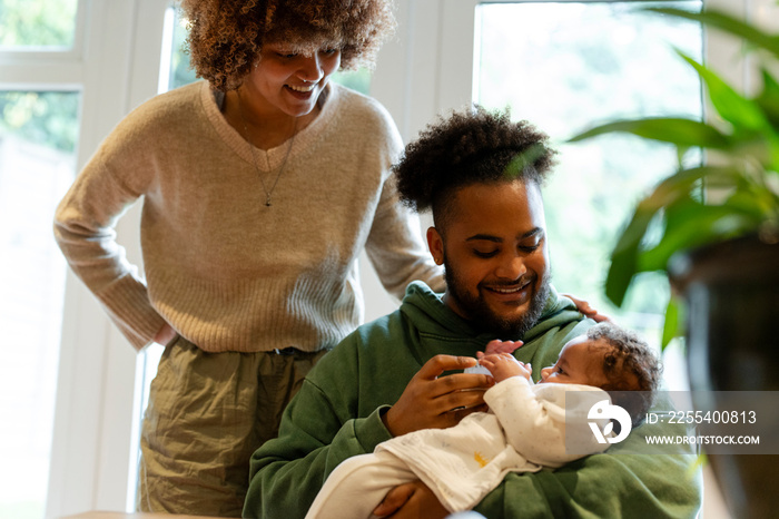 Mother looking at father feeding baby daughter at home