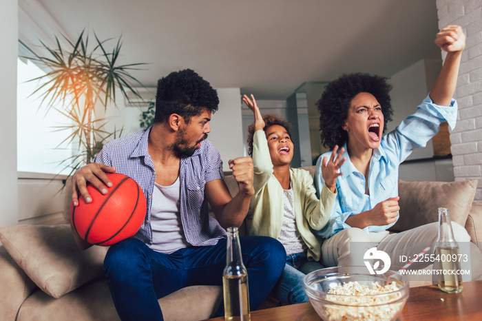 Happy African American family of three watching tv and cheering sport games on sofa at home