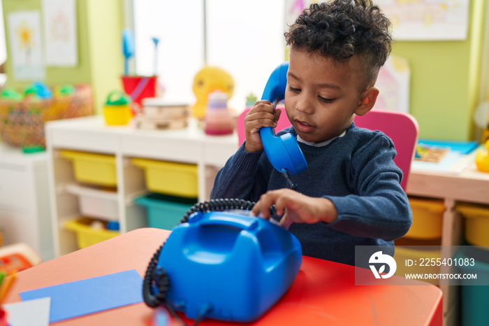 African american boy playing telephone toy sitting on table at kindergarten