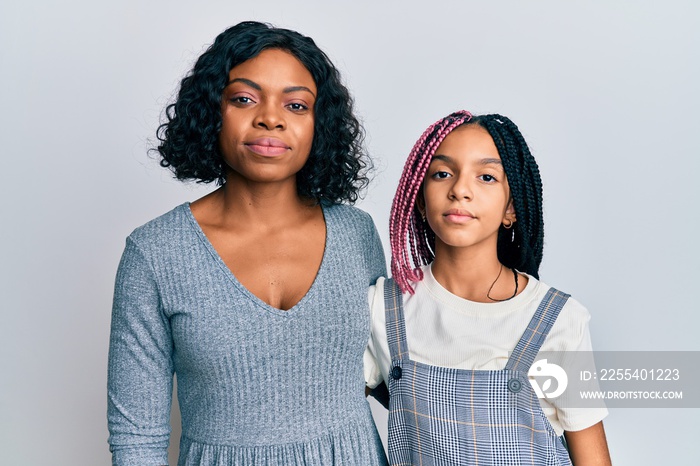 Beautiful african american mother and daughter wearing casual clothes and hugging relaxed with serious expression on face. simple and natural looking at the camera.