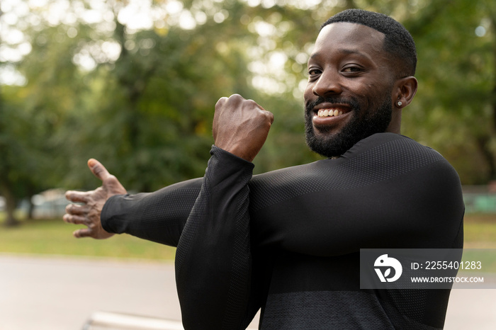 Portrait of smiling athletic man stretching arm in park