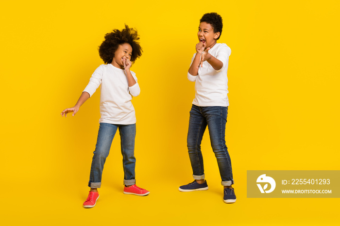 Full body portrait of carefree positive siblings sing arm imagine microphone isolated on yellow color background