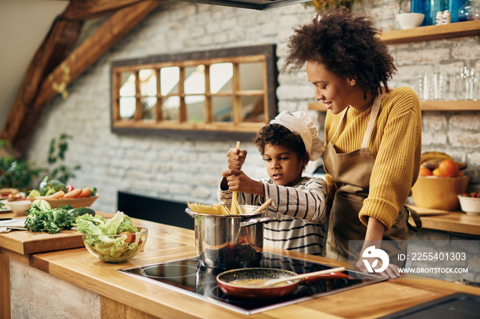 Small black boy cooking spaghetti with his mother in the kitchen.