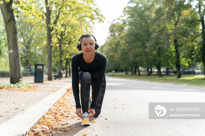 Portrait of woman in sports clothing and headphones tying shoe in park