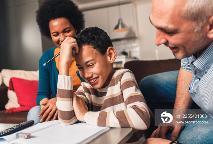 Parents helping their son with his homework at home in living room.