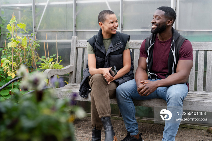 Smiling couple relaxing on bench in front of greenhouse