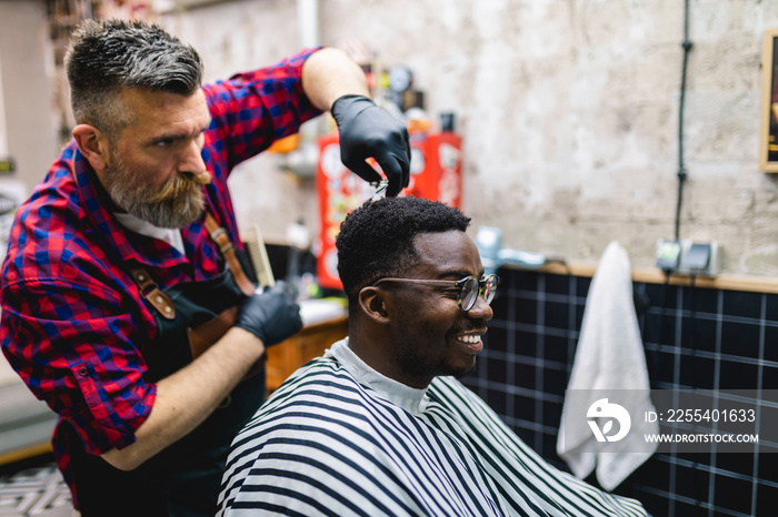 Young African man visiting hairstylist in barber shop. Professional hairdresser cut hair with scissors.