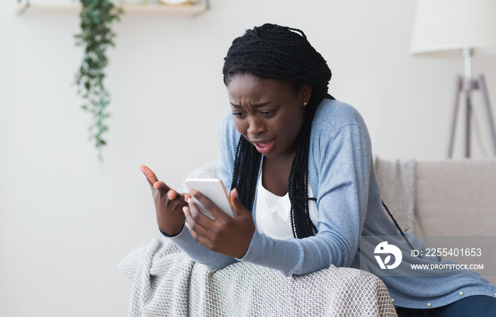 Frustrated black woman having problems with smartphone at home