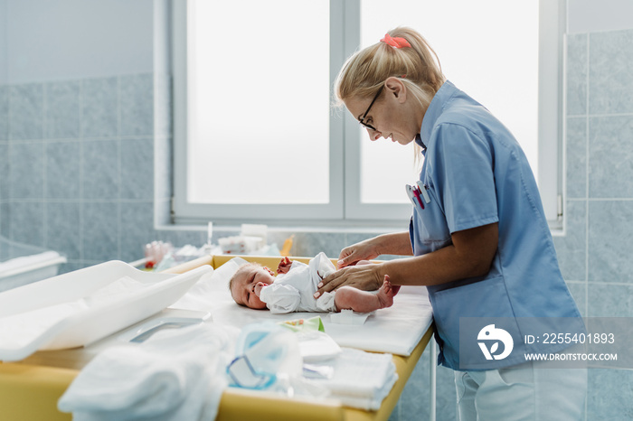 Young nurse working in maternity ward. She is wrapping the newborn baby.