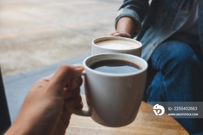 Closeup image of a couple people clinking coffee cups together in cafe