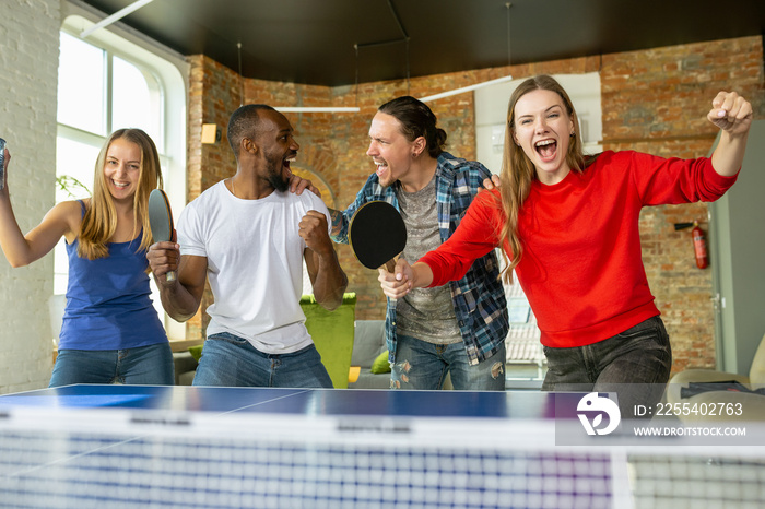 Young people playing table tennis in workplace, having fun. Friends in casual clothes play ping pong together at sunny day. Concept of leisure activity, sport, friendship, teambuilding, teamwork.