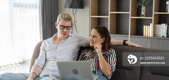 Caucasian couple talking and looking on laptop together in the living room. woman eating snack watching movie, online shopping or video call with family. relaxing on weekend at home