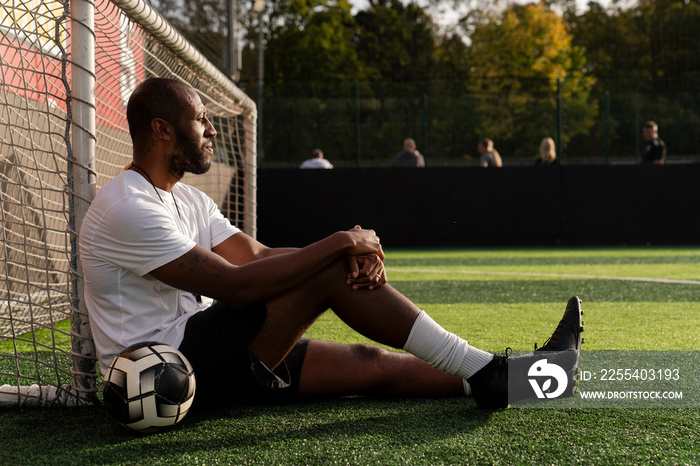 Man with ball sitting next to soccer goal