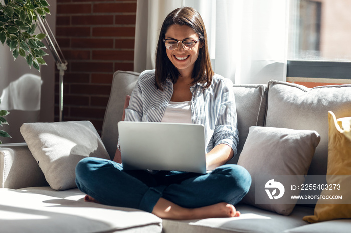 Pretty young woman working with her laptop while sitting on couch at home.