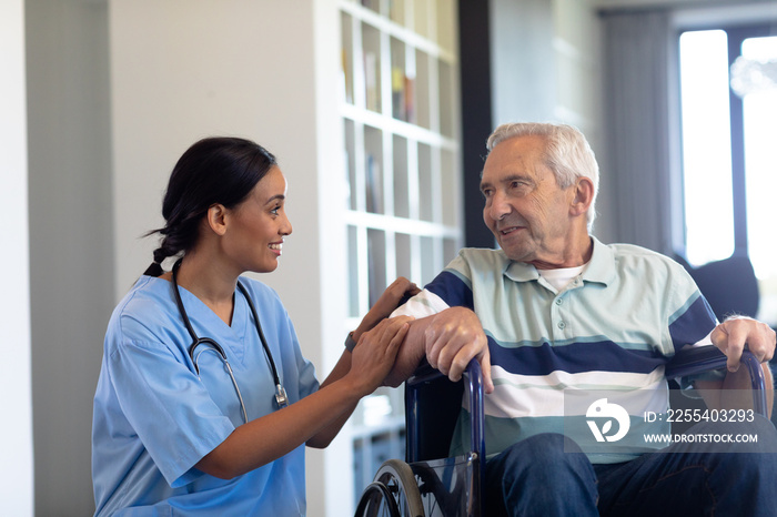 Smiling biracial female physiotherapist talking with caucasian senior man sitting on wheelchair