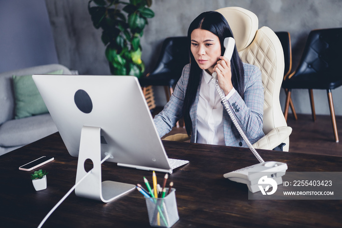 Portrait of serious lady sitting chair speak communicate phone look screen wear grey jacket indoors