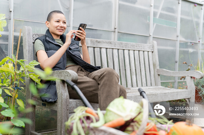 Smiling woman with smart phone in vegetable garden