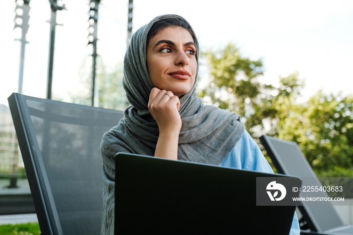 Young muslim woman wearing headscarf using laptop while sitting outdoor