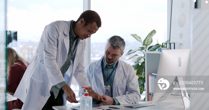 Multi-ethnic ocuple of doctors collaborating in medicla private clinic oiffice using computer discussing diagnosis examine symptoms of influenza.