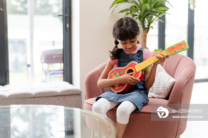 Little girl playing on ukulele in living room