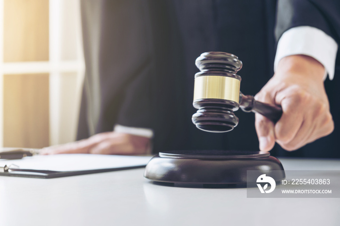 Close up of Male lawyer or judge hand’s striking the gavel on sounding block, working with Law books, report the case on table in modern office, Law and justice concept