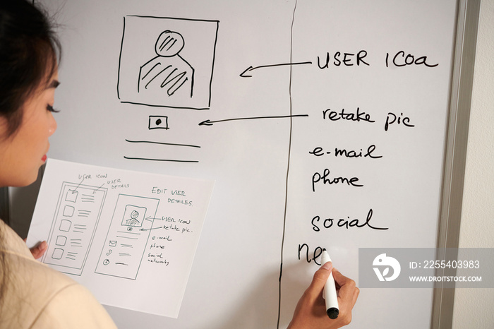 UX designer writing ideas for improving mobile application interface on whiteboard