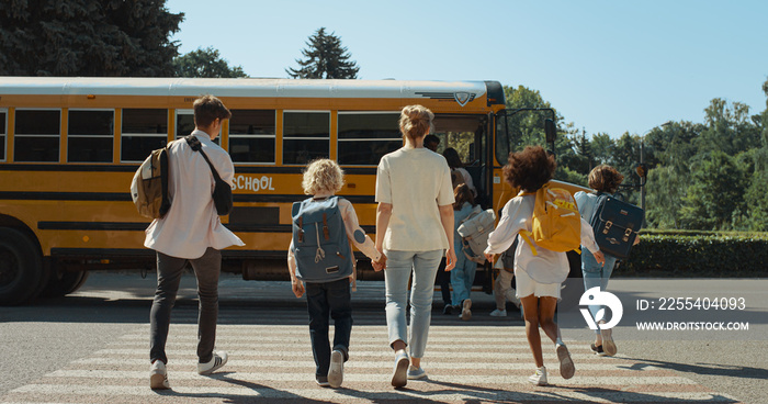 Mother hold hand schoolboy walking to bus. Energetic pupils running crossway.