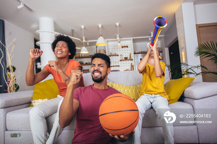 Happy African American family watching tv and cheering basketball games on sofa at home.