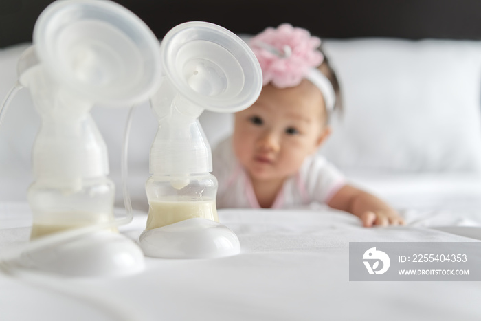 Breast milk in milk pump’s bottles on the bed with little cute baby crawling in background. The milk got from the pump’s machine and ready for the baby. Focus on milk bottle. Baby health care concept