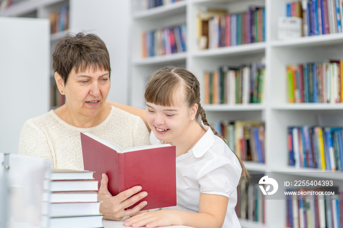 Mother and her daughter with syndrome down read a book at library. Education for disabled children concept