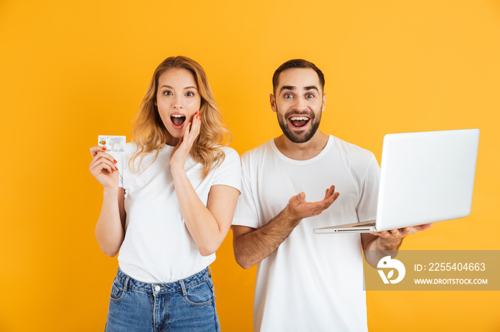 Image of impressed couple man and woman expressing surprise together while holding laptop and credit card