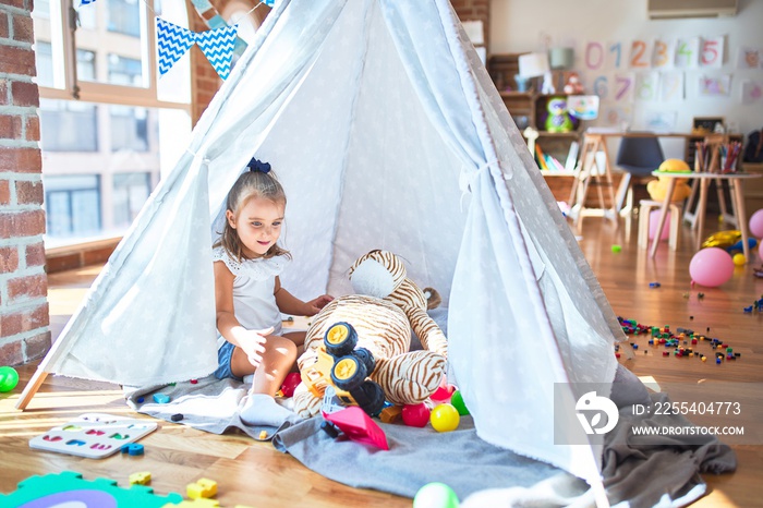 Young beautiful blonde girl kid enjoying play school with toys at kindergarten, smiling happy playing inside indian tent at home