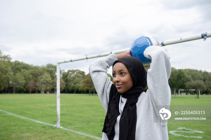 Smiling woman in hijab throwing soccer ball in park