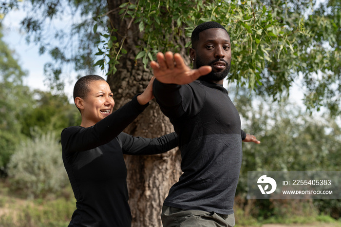 Yoga instructor assisting man practicing yoga in park