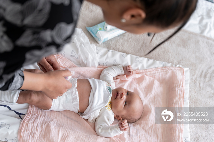 Mother changing diaper to newborn baby girl on bed at home