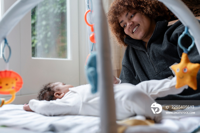 Smiling mother looking at baby daughter lying on play mat at home